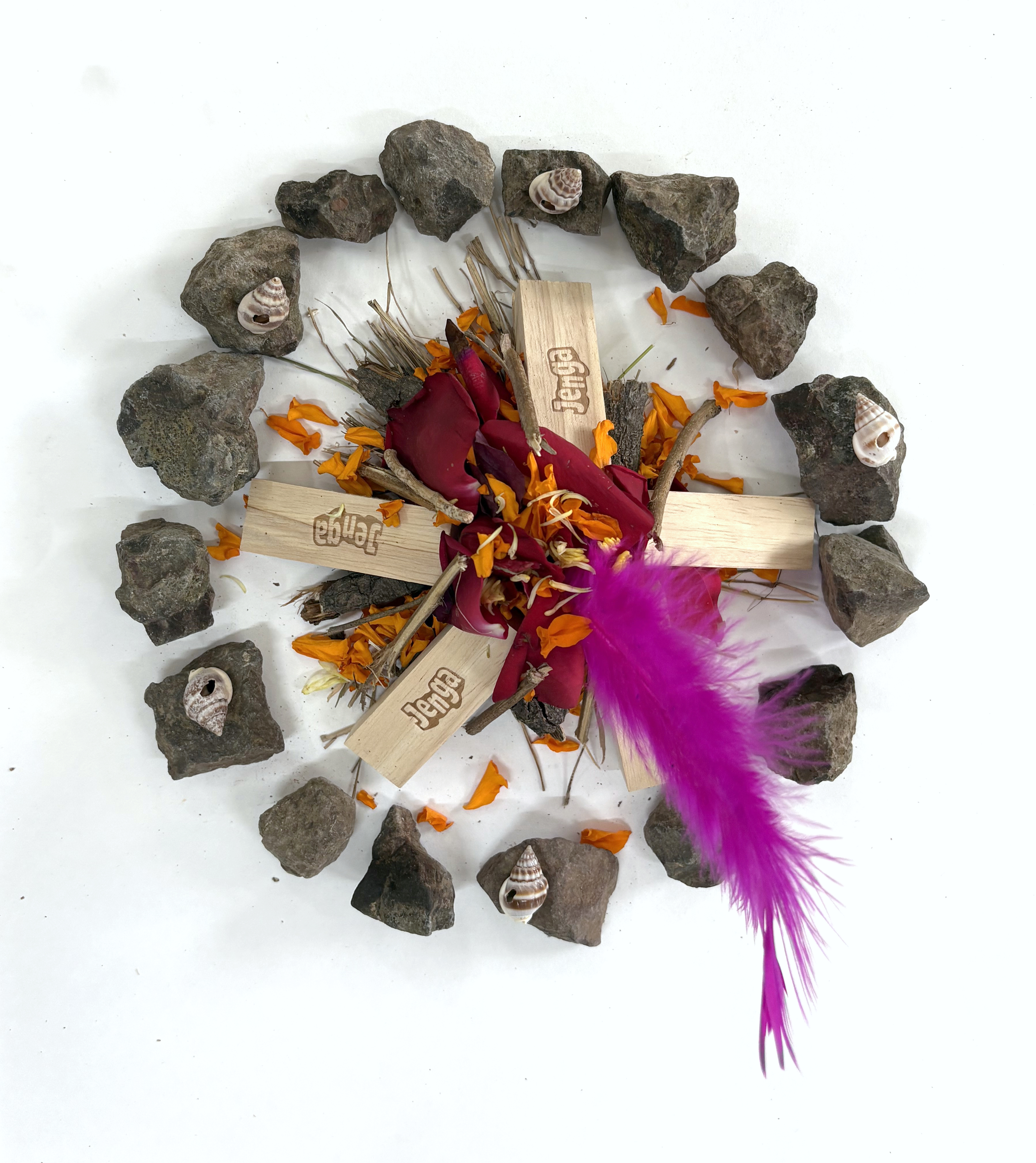 Mandala of stones, flowers, shells and a feather arranged around wooden blocks